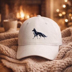 May include: A white baseball cap featuring a black and white stylized dog graphic. The cap has a curved brim and a button on top. The hat is sitting on a soft, textured surface.