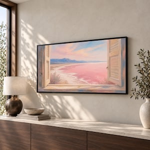 May include: A rectangular wall art print in a black frame depicting an open window view of a pink lake, a sandy shoreline, and distant mountains under a soft pastel sky. The scene features wooden shutters on both sides of the window frame.