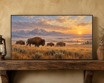 May include: A rectangular framed wall art print depicting a landscape scene with four bison grazing in a golden grassy field. In the background, snow-capped mountains rise above a misty valley under a vibrant orange and yellow sunset sky.