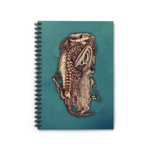 Puede incluir: Cuaderno de espiral con una ilustración detallada de un esqueleto de dinosaurio y una criatura peluda. La obra de arte está en tonos marrones y beige sobre un fondo turquesa. El cuaderno tiene una encuadernación en espiral negra.