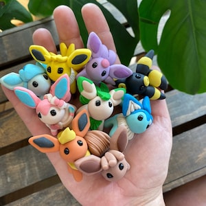 May include: A collection of nine small, hand-crafted clay figurines of Pokemon characters. The figurines are painted in various colors, including blue, yellow, green, and brown.