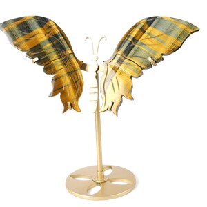 May include: A butterfly ornament with outstretched wings. The wings display a gold and black striped pattern. The butterfly is supported by a gold-coloured metal stand with a circular base. The wingspan is approximately 20 cm.
