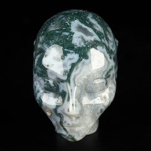May include: A green and white agate skull carving. The skull is polished and has a smooth, rounded surface. The agate is a natural stone with a unique pattern of green and white.