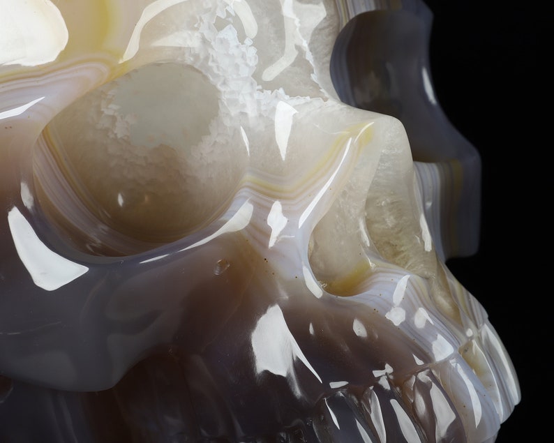 May include: A detailed carving of a human skull made from agate. The skull is translucent and shows the natural banding of the agate in shades of white, grey, and brown.