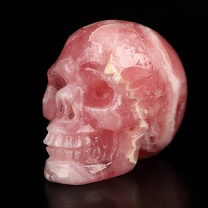Könnte beinhalten: Ein rosa Kristallschädel, geschnitzt aus Rosenquarz. Der Schädel ist detailliert und hat eine glatte, polierte Oberfläche.