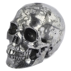 May include: A black and silver skull sculpture made of pyrite, a mineral known for its metallic luster. The skull is detailed with a textured surface and a defined jawline.