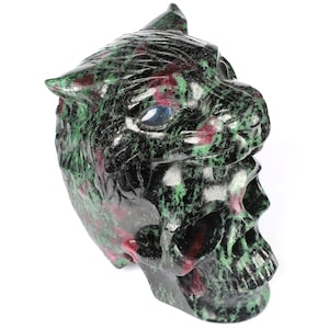 May include: A green and red gemstone skull with a carved tiger face on top. The skull has blue eyes and is made of a polished stone.