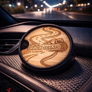 May include: A car air freshener with a wooden top featuring a road design and the text "TRACK SCENTS". The air freshener is in a black container, sitting on a car dashboard. The background shows a blurred night scene with streetlights.