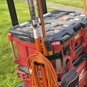 May include: Red and black rolling tool storage system with orange extension cords and tools. The system includes a black and red toolbox, a black tool bag, and two orange poles. The system is on a grassy surface.