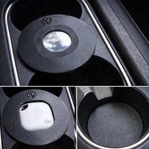 Op de afbeelding: Zwarte auto bekerhouder inzet met een textuur. De inzet heeft een cirkelvormig ontwerp met een logo en een centrale opening. Een witte Tile tracker is te zien in de inzet. De bekerhouder zit in een auto.