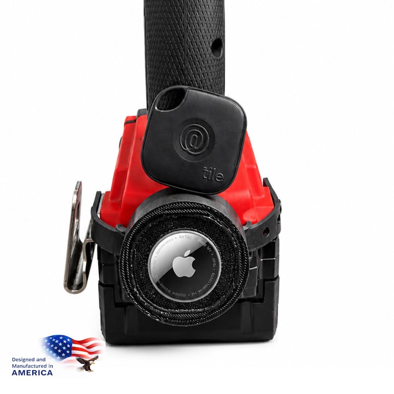 May include: A black Tile tracker and an Apple AirTag are shown on a red and black object. The Tile tracker has an @ symbol and the word "tile". The AirTag has the Apple logo. The image also includes the text "Designed and Manufactured in AMERICA" with an American flag.