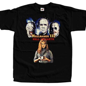 Może przedstawiać: Czarny t-shirt z krótkim rękawem z nadrukiem graficznym z filmu Hellraiser III: Hell on Earth. Wzór przedstawia trzy postacie z horroru nad tytułem filmu oraz osobę trzymającą w dłoniach kostkę logiczną na środku.