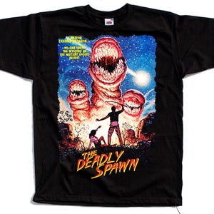 Könnte beinhalten: Schwarzes T-Shirt mit einem farbenfrohen Grafikdesign von "The Deadly Spawn". Das Design zeigt ein Monster mit großen Zähnen, einen Sternenhimmel und den Text "The Deadly Spawn". Das Shirt hat auch Text, der lautet: "Ein Meteor stürzte auf die Erde... Niemand kannte die Geheimnisse der Mutanten-Sporen im Inneren!"
