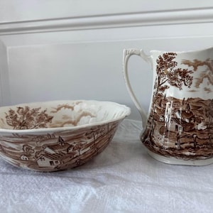 May include: A white ceramic mug with a black handle and the text "But First, Coffee" in a bold, black font. The mug is set against a blurred background, highlighting its clean design.