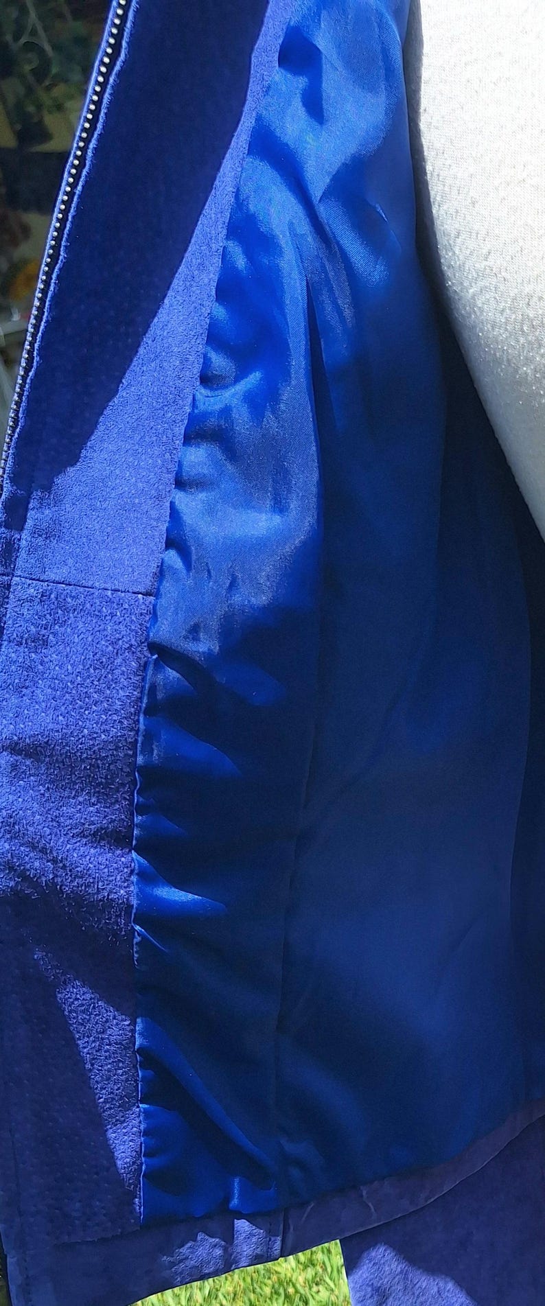 May include: A vibrant royal blue jacket featuring a textured suede-like outer material and a smooth, matching blue satin-finish lining. The garment includes a vertical zipper closure along the front edge, showcasing the contrast between the matte exterior.