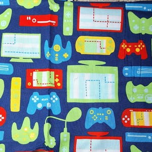 May include: A dark blue fabric featuring a repeating pattern of colorful video game consoles, handheld gaming devices, and controllers in shades of lime green, bright red, yellow, and light blue, with white screen details on the devices.