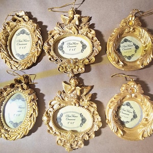 May include: Six gold-colored hanging photo frame ornaments with ornate, detailed borders. The frames feature various shapes including oval and circular designs, some topped with cherub figures. Each frame contains a paper insert labeled Photo Frame Ornament with dimensions listed in inches.