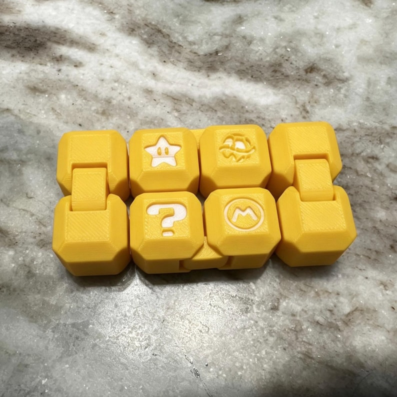 May include: Yellow, interlocking toy blocks featuring white symbols including a star, a question mark, a turtle, and an "M" in a circle. The blocks are linked together.