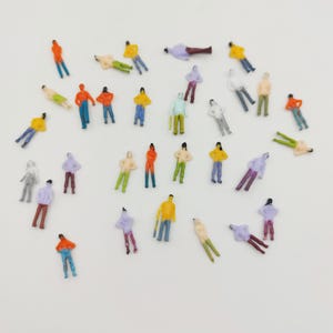 May include: Miniature figurines of people in various poses and colorful outfits. The figures are dressed in a variety of colors, including orange, yellow, blue, green, and purple. Some figures are standing, while others are lying down.