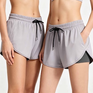 May include: Two pairs of light gray athletic shorts with a black drawstring and a matching sports bra. The shorts have a loose fit and a built-in liner. The shorts are designed for athletic activities.
