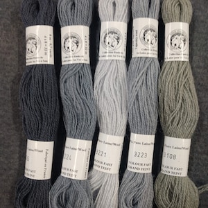 May include: Five skeins of wool yarn in different shades of gray and green. The yarn is labeled with the brand name "Laine/Wool" and the color numbers 3108, 3223, 3221, 224, and 6. The yarn is made in France and is colorfast.