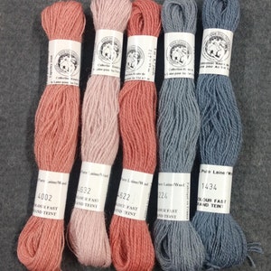 May include: Four skeins of wool yarn in shades of coral, pink, light blue, and dark blue. Each skein has a label with the brand name "Wine Italie", the color number, and the text "Pure Laine/Wool Colour Fast and Teint".