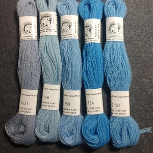 May include: Five skeins of wool yarn in shades of blue. The yarn is labeled with the brand name "Fink Tha" and the color numbers 1421, 148, 150, 2154, and 2152. The yarn is described as "Pure Laine/Wool" and "Colour Fast/Grand Teint".