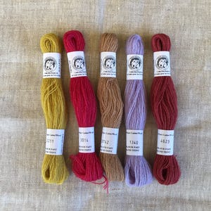 May include: Five skeins of wool embroidery thread in mustard yellow, deep red, tan, light lavender, and dark red. Each skein features a white paper label with the text 'Collection Fleur de Lin', 'Pure Laine/Wool', and specific color numbers.
