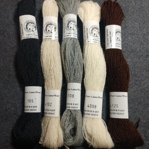 May include: Five skeins of wool yarn in black, white, gray, white, and brown. The yarn is labeled with the brand name "Fine Dauphine" and the text "Pure Laine/Wool" with a number and the words "Colour Fast and Teint".