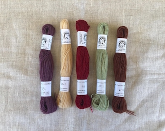 Può includere: Cinque matasse di pura lana nei colori viola scuro, beige chiaro, rosso scuro, verde salvia e marrone. Ogni matassa è fissata con un'etichetta di carta bianca con un logo circolare e testo stampato che include i numeri 2454, 2542, 946, 2132 e 4216.