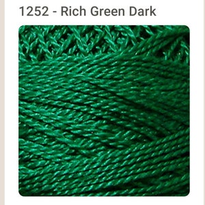 May include: A close-up of a spool of dark green yarn. The yarn is twisted and has a shiny finish.