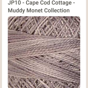 May include: Close-up of a skein of yarn in a muted purple shade. The yarn is textured and has a subtle sheen. The yarn is labeled "JP10 - Cape Cod Cottage - Muddy Monet Collection".