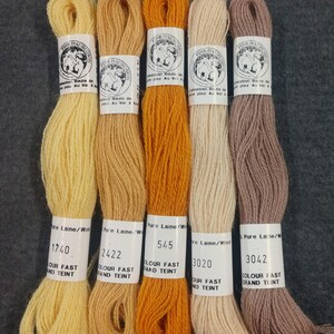 May include: Five spools of embroidery floss in shades of yellow, orange, beige, and brown. The spools are labeled with the brand name "Fine Daubuisson" and the color numbers 1740, 2422, 545, 3020, and 3042. The spools are labeled "Pure Laine/Wool" and "Colour Fast Grand Teint."