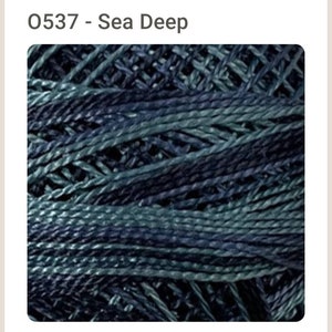 May include: Close-up of a skein of yarn with a sea-deep color gradient. The yarn is a blend of dark teal, navy, and lighter blue-green hues, creating a textured, layered appearance. The text "O537 - Sea Deep" is at the top.