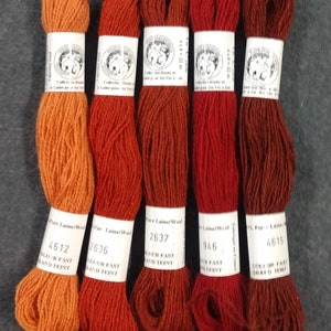 May include: Five spools of embroidery floss in shades of orange, red, and brown. The spools are labeled with the brand name "Laine" and the color numbers 4612, 2636, 2637, 946, and 4615. The spools are all labeled "Pure Laine/Wool" and "Colour Fast and Teint".