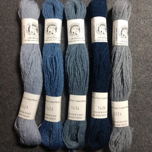 May include: Five skeins of wool yarn in shades of blue and gray. The yarn is labeled with the numbers 1421, 1423, 1434, 1436, and 3224. Each skein is labeled "Pure Laine/Wool" and "Colour Fast Grand Teint".
