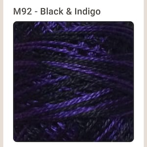 May include: Close-up of a skein of yarn with black and indigo blue threads. The yarn is tightly wound and the colors are vibrant.