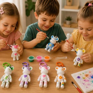 May include: A set of white bear-shaped plastic keychains with attached colorful plastic clips, featuring various hand-painted designs including hearts, flowers, and rainbows, accompanied by small paint pots and brushes for creative decoration.