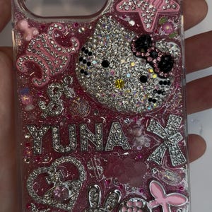 Pu&ograve; includere: Custodia trasparente per telefono con glitter rosa e abbellimenti di strass. Presenta un Hello Kitty ricoperto di strass, il nome "YUNA" in strass e vari ciondoli, tra cui stelle, fiocchi e un coniglietto. La custodia &egrave; progettata per uno smartphone.