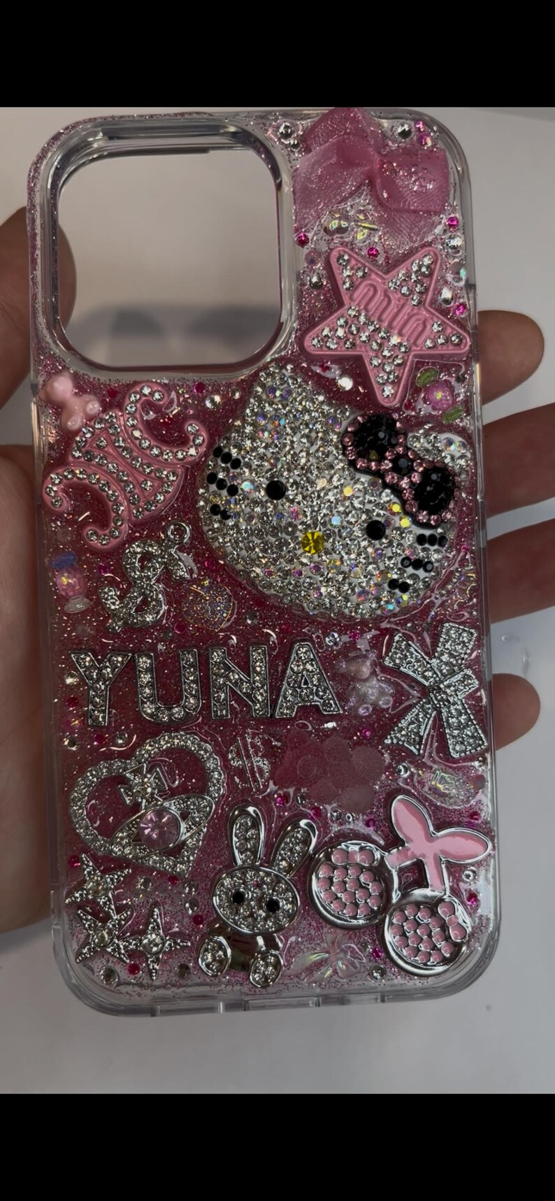 Pu&ograve; includere: Custodia trasparente per telefono con glitter rosa e abbellimenti di strass. Presenta un Hello Kitty ricoperto di strass, il nome "YUNA" in strass e vari ciondoli, tra cui stelle, fiocchi e un coniglietto. La custodia &egrave; progettata per uno smartphone.