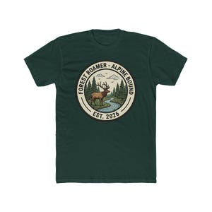 May include: Dark green t-shirt featuring a circular graphic with a deer, river, and trees. The text reads "FOREST ROAMER - ALPINE BOUND" and "EST. 2026". The design is in shades of brown, green, and blue.