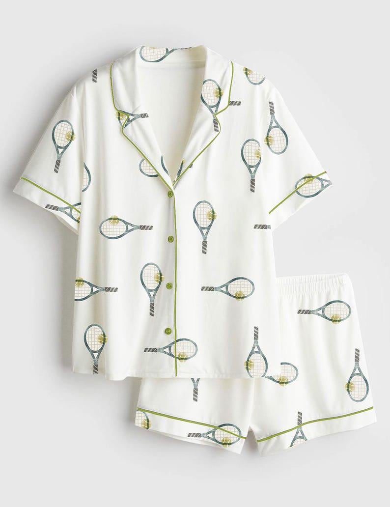 May include: White pajama set featuring a tennis racket pattern in blue and yellow. The short-sleeved top and shorts have green trim. The button-down shirt has green buttons.