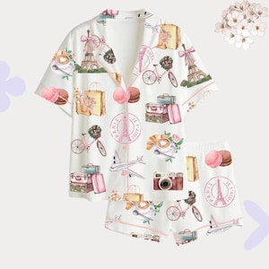 May include: White pyjama set with a repeating pattern of Parisian imagery, including the Eiffel Tower, bicycles, suitcases, and macarons. The set features a button-down top and shorts, trimmed with pink piping.