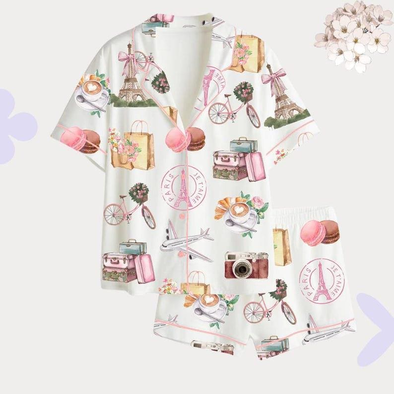May include: White pyjama set with a repeating pattern of Parisian imagery, including the Eiffel Tower, bicycles, suitcases, and macarons. The set features a button-down top and shorts, trimmed with pink piping.
