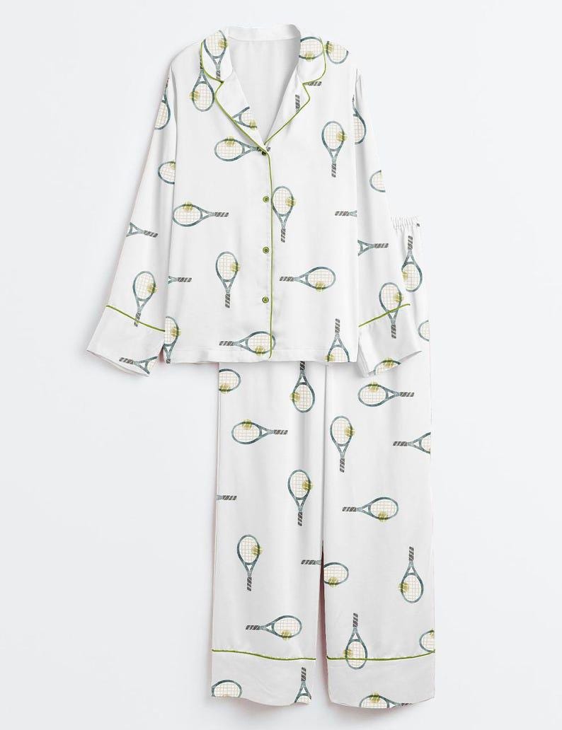 May include: White pajama set with a tennis racket pattern. The long-sleeved top has a button-down front and green trim. The matching pants also feature the tennis racket design and green trim.