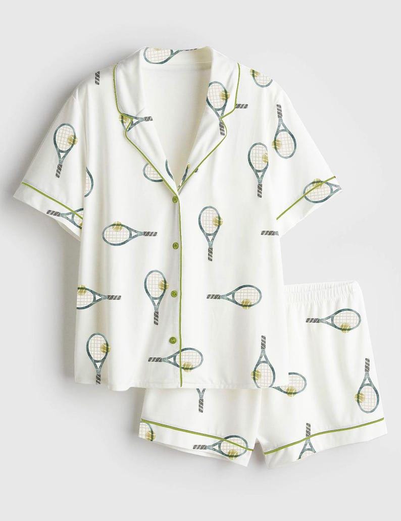 May include: White pajama set featuring a tennis racket pattern in blue and yellow. The short-sleeved top and shorts have green trim. The button-down shirt has green buttons.