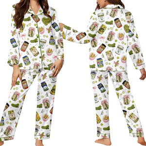 May include: White pajama set with a repeating pattern of pickle jars, pickles, and pink bows. The long-sleeved top and pants have green trim. The pajama set is made of a soft, comfortable material.