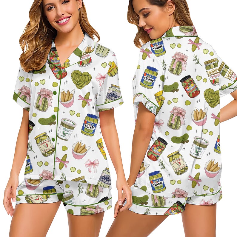 May include: White pajama set with a pickle pattern. The short-sleeved top and shorts feature illustrations of pickles, jars, and pink bows. Green trim outlines the edges of the pajamas.