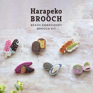 Könnte beinhalten: Eine Sammlung von Broschen-Kits mit Perlenstickerei und Food-Designs. Die Broschen zeigen Eis am Stiel, Brot und andere Lebensmittel. Der Text "Harapeko BROOCH" ist über den Broschen zu sehen.