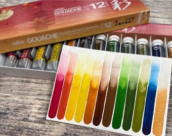 Puede incluir: Un juego de 12 tubos de pintura Gouache Holbein Artists en una caja, con una tarjeta de muestra de color que muestra la gama de colores. La caja es naranja y roja con texto japonés. La tarjeta muestra un espectro de colores.